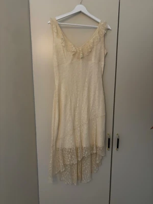 Krämvit spetsklänning med volang - Romantisk krämvit klänning i spets med volangdetalj vid ringningen och asymmetrisk fåll. Ärmlös modell med vacker struktur och lätt transparent nederdel. Perfekt för sommarens alla tillfällen och ger en bohemisk känsla. Nypris 400, aldrig använd 