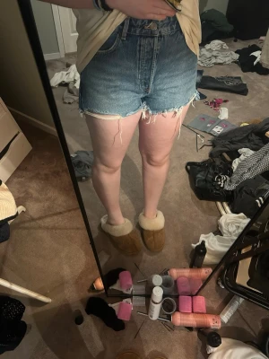 Högmidjade blå jeansshorts - Säljer ett par klassiska blå jeansshorts med hög midja och råa, fransiga benslut. Shortsen har fem fickor och en avslappnad passform som ger en chill vibe. Perfekta för sommardagar och enkla att matcha med allt.