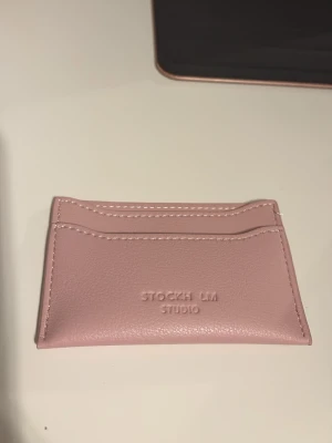 Rosa kortfodral från Stockh LM Studio - Säljer ett stilrent rosa kortfodral från Stockh LM Studio. Kortfodralet har flera fack för kort och är gjort i ett slätt, veganskt lädermaterial. Perfekt för dig som vill ha ett smidigt och snyggt sätt att förvara dina kort.