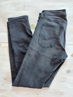 Svarta slim fit jeans från Lee - Snygga svarta slim fit jeans från Lee med klassisk femficksmodell och diskreta slitningar. Jeansen har normal midja och raka ben, tillverkade i mjuk bomullsdenim med lite stretch för extra komfort.