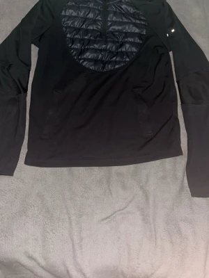 Svart Nike Therma-Fit tröja XL - Säljer en svart långärmad Nike Therma-Fit tröja i storlek XL barn. Tröjan har en quiltad panel framtill, halv dragkedja och två sidofickor. Perfekt för träning eller utomhusaktiviteter när det är kallare. Materialet är en mix av syntet och vadderad front.