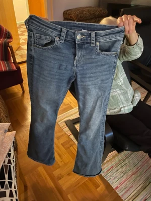 Blå bootcut jeans med fickdetaljer - Snygga blå bootcut jeans med klassisk femficksdesign och knappar på bakfickorna. Jeansen har en lätt tvättad look och raka ben med lite utsvängd passform. Perfekta för en avslappnad och trendig stil.
