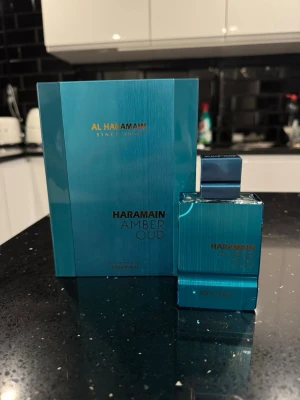 Al Haramain Amber Oud Aqua Parfym - Fräsch parfym från Al Haramain i serien Amber Oud. Flaskan är fyrkantig och har en metallicblå färg med guldfärgad text. Kommer i matchande blå förpackning. Doften är Aqua och flaskan har en modern, stilren design.