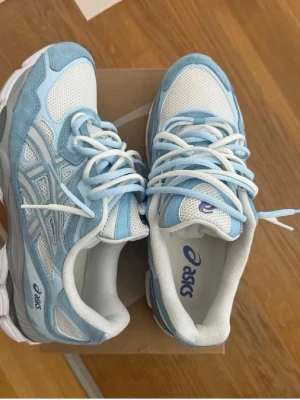 Asics vita och ljusblå sneakers - Snygga sneakers från Asics i vitt och ljusblått med meshpaneler och detaljer i syntet. Skorna har en chunky sula och klassisk snörning. Perfekta för dig som gillar sportig och trendig stil.