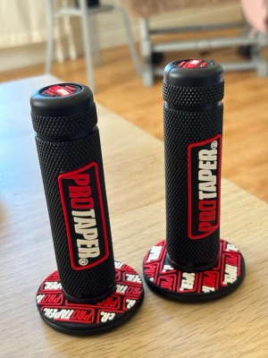 ProTaper svarta handtag motocross - Säljer ett par svarta handtag från ProTaper med röd och vit logga. Handtagen har greppvänlig yta och rundad kant med tryckt mönster i rött, vitt och svart. Perfekt för motocross eller cykelstyre.