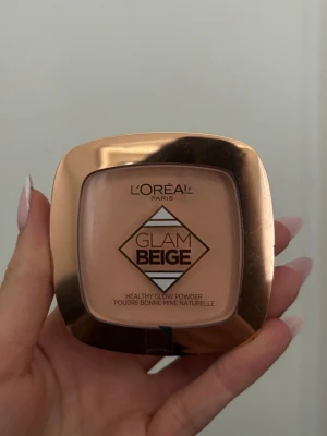 L'Oréal Glam Beige Healthy Glow Powder - L'Oréal Glam Beige Healthy Glow Powder i en snygg beige nyans. Kompakt puder i fyrkantig dosa med spegel och guldfärgat lock. Ger en naturligt fräsch finish och passar perfekt för att jämna ut hudtonen. Innehåller 9g och är enkel att ta med i väskan.
