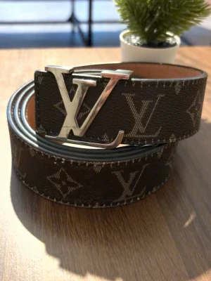 Klocka  - Snyggt brunt bälte med klassiskt -monogram och stor silvrig -spänne framtill. Bältet har en exklusiv känsla och är gjort i skinn med beige insida. Perfekt accessoar för att lyfta din outfit.