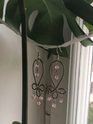 Silvriga örhängen med rosa pärlor - Mina handgjorda örhängen.  Rosa pärlor på silverfärgad metalltråd.  Nickelfria!  Följ min Instagram för mer <3 @veras.smycken.  Unika örhängen i silverfärgad metall med en elegant, böjd form och små rosa pärlor som hänger i olika nivåer. Designen har en öppen, droppformad siluett med dekorativa detaljer längst ner. Perfekta för dig som gillar statement-smycken med en feminin touch.