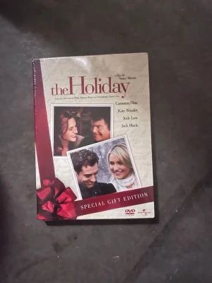 The Holiday Special Gift Edition DVD - Säljer en DVD-box av filmen The Holiday, Special Gift Edition. Omslaget är beige med röda detaljer och bilder på skådespelarna. Perfekt för dig som gillar romantiska komedier och samlar på filmer.