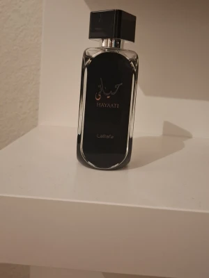 Hayaati parfym från Lattafa - Säljer en elegant parfymflaska från Lattafa, modellen Hayaati. Flaskan är svart med silverdetaljer och har en modern, rektangulär form med rundade kanter och svart fyrkantigt lock. Perfekt för dig som gillar stilrena och exklusiva dofter. Nästan allt kvar