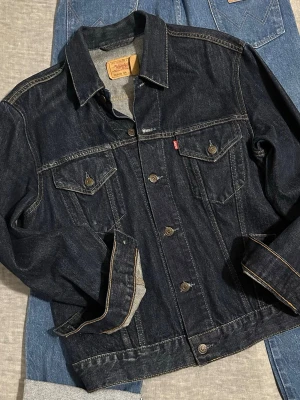 🔥Levi’s 70500 Dark Indigo Trucker Jacket XL – Made in Italy - Levi’s 70500 trucker jacket in deep dark indigo denim. Made in Italy (01/2016 production).  Size XL – structured fit, works great oversized. Classic Type III cut with clean lines and strong denim feel. Light natural wear and subtle distress details. No major flaws.  Timeless staple piece. Easy to style with cargos, denim or hoodie layering. Measurements waist 49cm, length 67cm, p2p 56cm, s2s 50cm, sleeve 65cm Condition: Good – worn but well kept.