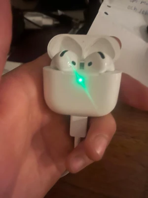 Trådlösa vita hörlurar med laddningsetui - Säljer ett par trådlösa vita hörlurar från Apple, modell AirPods, med tillhörande laddningsetui. Hörlurarna har en stilren och kompakt design i blank plast och laddas via Lightning-kabel. Perfekta för musik, samtal och poddar. AirPods 4 PRO 
