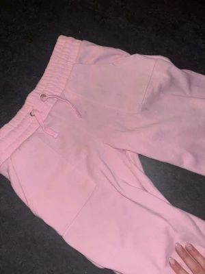 Söta rosa lågmidjade mjukisbyxor den lager157 - Säljer ett par ljusrosa mjukisbyxor med bred resår i midjan och dragsko. Byxorna har stora fickor framtill och är gjorda i mjukt bomullsliknande material. Perfekta för chill dagar och riktigt sköna att ha på sig.