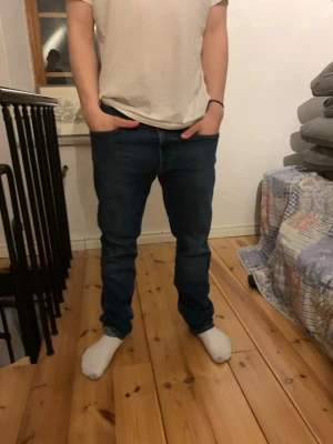 Mörkblå slim fit jeans herr - Säljer ett par mörkblå slim fit jeans med klassisk femficksdesign och normal midja. Jeansen har en snygg, enkel look och sitter tight över benen utan att bli för smala. Perfekta till en avslappnad stil och passar till det mesta.