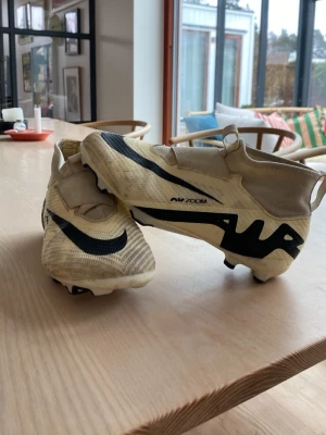 Nike Air Zoom vita fotbollsskor - Säljer ett par vita Nike Air Zoom fotbollsskor med svarta detaljer och snörningsfritt överdrag. Skorna har en modern, strömlinjeformad design och är tillverkade i syntetmaterial för bästa grepp och känsla på planen. Perfekta för dig som vill ha stil och prestanda på matchen.