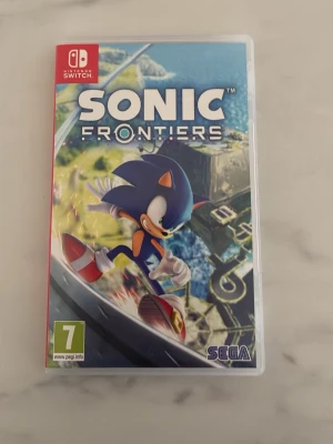Sonic Frontiers till Nintendo Switch - Sonic Frontiers till Nintendo Switch är ett actionfyllt äventyrsspel där du utforskar öppna världar med Sonic. Omslaget är färgglatt med Sonic i blått och rött, och spelet bjuder på snabba plattformsmoment och nya strider. Perfekt för dig som gillar fart och utmaningar.