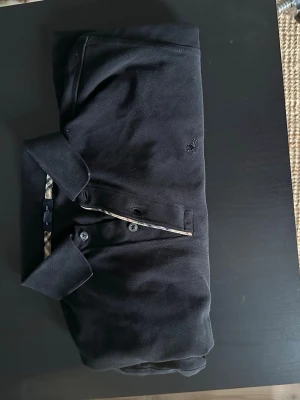 långärmad Burberry piké - Säljer en svart långärmad piké från Burberry. Pikén har diskret Burberry-logga på bröstet och detaljer i det ikoniska rutmönstret vid kragen. Ställ frågor vid minsta funderingar😁