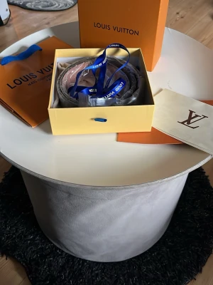 Belt Louis Vuitton  🌟 - This Louis Vuitton belt features the iconic Damier pattern with a silver LV buckle. The leather appears well-maintained.  ⭐️ Condition: 10/10  🎨 Color: Grey and Black 📦 Fast and careful shipping. OBS BOX KAN MEDFÖLJA FÖR EXTRA KOST!