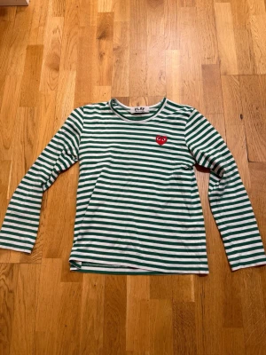 Randig långärmad topp Comme des Garçons - Säljer Grön- och vitrandig långärmad topp från Comme des Garçons Play med det ikoniska röda hjärtat. Den passa inte mig så vill sälja den vidare S/Xs