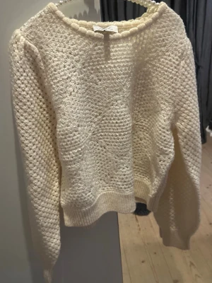 Vit stickad tröja med strukturmönster - Säljer en krämvit stickad tröja med snyggt strukturmönster och rund hals. Tröjan har ballongärmar och ribbade muddar vid ärmslut och nederkant. Perfekt till jeans för en chill look.