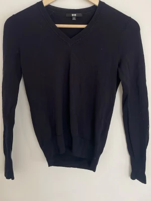 Mörkblå V-ringad tröja från Uniqlo - Klassisk tajt mörkblå tröja från Uniqlo med V-ringning och långa tajta ärmar. Tillverkad i ett mjukt och tunt material. Enkel och stilren design med ribbade muddar vid ärmslut och nederkant❣️                                                            Ett hål på ena ärmen, ca 1 cm (se bild)