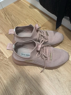 Rosa sneakers från Steve Madden - Snygga rosa sneakers från Steve Madden med stickad ovandel och matchande snören. Skorna har detaljer i guld på snörningen och en elastisk hälflik med logga. Lätta och flexibla med sportig look och modern design.