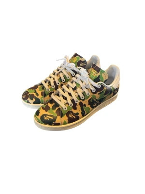 Adidas x Bape camo Stan Smith - Unika sneakers från Adidas i samarbete med Bape. Klassisk Stan Smith-modell med grön, brun och svart camo-mönster över hela skon och vita detaljer. Låga med vita snören och sula. Perfekt för dig som vill sticka ut med streetwear-vibe.