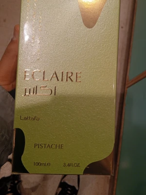 Lattafa Eclaire Pistache parfym 100ml - Lattafa Eclaire Pistache är en parfym i en elegant grön och guld kartong. Doften har pistage som huvudtema och flaskan rymmer 100 ml. Förpackningen har en lyxig känsla med gulddetaljer och modern design.