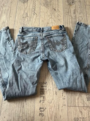 Wrangler ljusblå raka jeans - Säljer ett par ljusblå flared jeans från GinaTricot i flared ben och klassisk femficksmodell. Jeansen har  broderade detaljer på bakfickorna, detaljer på benen och med en läderpatch med logga i linningen. De är lågmidjade.