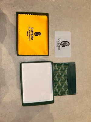 Grön korthållare från GY - Snygg grön korthållare från GY med det klassiska mönstret i vitt och grönt. Tillverkad i canvas och läder, har flera fack för kort och levereras med original ask, putsduk och certifikat. Perfekt för dig som vill ha något exklusivt och stilrent i fickan.