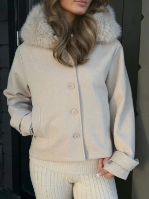 Beige vårjacka - Stilren beige kappa med stor fluffig fuskpäls-krage och raka ärmar. Två knappar vid luvan har tyvärr försvunnit när jackan köptes annars är den som ny💗perfekt nu till våren