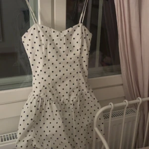 Vit prickig sommarklänning från Bershka  - Vit kortklänning med svarta prickar och smala axelband. Klänningen har en lätt utställd kjol och är ärmlös, vilket gör den luftig och bekväm. Perfekt för varma dagar och tillverkad i ett mjukt bomullstyg💞💞