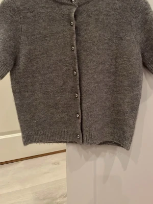 Grå kofta från Zara, S - Mysig grå kofta från Zara med rund halsringning och silvriga knappar framtill. Koftan är stickad i ett mjukt material och har ribbade muddar vid ärmslut och nederkant. Perfekt att slänga över en t-shirt eller topp för extra värme.