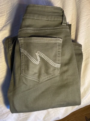 Olivgröna jeans från Nelly - Snygga olivgröna jeans från Nelly med vita kontrastsömmar och klassisk femficksdesign. Jeansen har en dekorativ söm på bakfickan och dubbla knappar i midjan. Perfekta för dig som vill ha en cool och avslappnad stil.