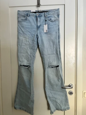 Ljusblå utsvängda jeans med slitningar - Snygga ljusblå jeans från lager 157 med utsvängda ben och slitna hål vid knäna. Klassisk femficksmodell och hög midja. Jeansen har en trendig vintagekänsla och är tillverkade i bomull. Perfekta för en avslappnad och cool stil. Aldrig använda❤️