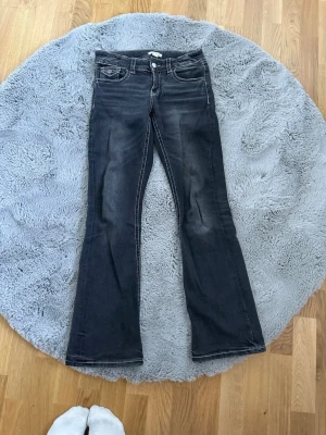 Mörkblå bootcut jeans med vita sömmar - Snygga mörkblå bootcut jeans med kontrasterande vita sömmar och klassiska fem fickor. Jeansen har lätt slitning framtill och bakfickor med lock och knapp. Perfekta för en avslappnad och trendig look.
