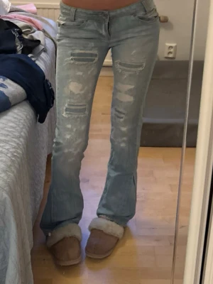 Ljusblå bootcut jeans med slitningar - Säljer ett par ljusblå bootcut jeans med  slitningar framtill. Jeansen har låg midja och är köpta second hand. Sydda till bootcut