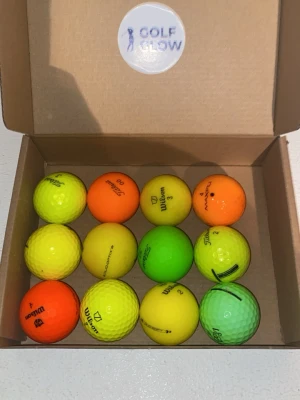 Färgmix 12-pack  - Säljer ett set med tolv golfbollar i olika färger som gul, orange och grön. Bollarna kommer i en enkel kartong med etiketten 'Golf Glow' på insidan av locket. Perfekt för dig som vill ha extra synliga golfbollar på banan.
