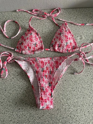 Blommig rosa bikini  - Söt bikini med blommigt mönster i rosa. Knytband i sidorna och nacken. Topp i triangelmodell och klassisk bikiniunderdel.