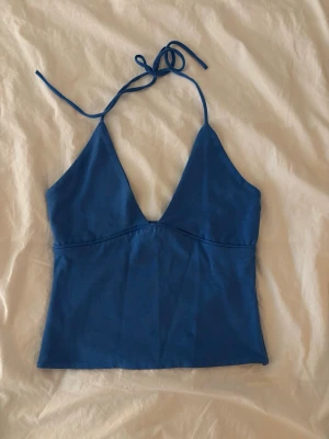 Blå halterneck linnetopp  - Snygg blå linnetopp med halterneck och djup v-ringning. Toppen har tunna knytband i nacken och är ärmlös, perfekt för varma dagar. Tillverkad i mjukt bomullsmaterial som känns skönt mot huden. Enkel och stilren design som passar till mycket. Använd fåtal ggr super bra skick! Från Gina tricot 14+❤️