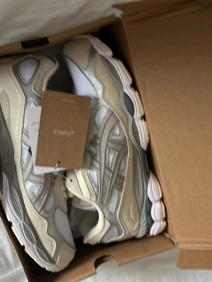 Asics gel nyc - Snygga Asics sneakers i beige, vitt och grått med meshpaneler och mockadetaljer. Skorna har en chunky sula och klassisk Asics-logga på sidan. Perfekta för dig som gillar stilrena och sportiga vibes.