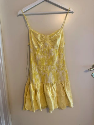 Gul och vit rutig sommarklänning - Söt kort gul och vit rutig klänning med volangkant och smala axelband. Klänningen har en rosett framtill och är perfekt för varma dagar. Lätt och luftig modell med omlottkänsla och feminina detaljer .