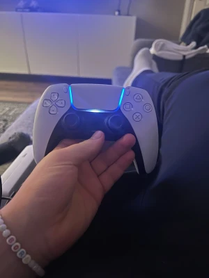  PlayStation 5 handkontroll - Säljer en vit PlayStation 5 DualSense handkontroll från Sony. Den har en futuristisk design med blå LED-belysning, klassiska PlayStation-knappar och greppvänliga svarta detaljer. Tillverkad i plast och passar perfekt för gaming på PS5. 