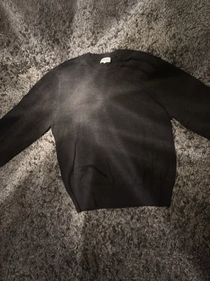 Mörkgrå stickad tröja från SANDÖ - En stilren svart stickad tröja från SAND med rund halsringning och långa ärmar. Tröjan har en klassisk rak passform och är perfekt för lager på lager. Materialet känns mjukt och bekvämt mot huden. Använd fåtal gånger så i princip nyskick. Ny pris ca 1000kr