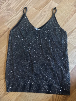 Glittrig festtopp - Snygg glittrig fest topp med silvriga nitar. Stretchig passform men sitter inte tight på kroppen. 