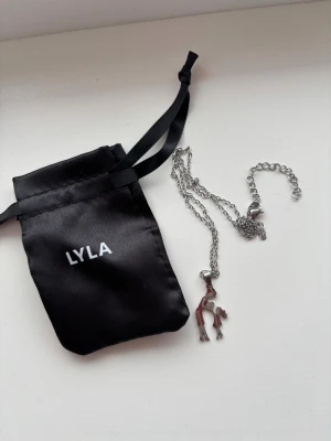 Silverfärgat halsband från LYLA - Säljer ett stilrent halsband i silverfärg från LYLA med en unik mamma och barn berlock Kedjan är tunn och har justerbar längd. Perfekt för dig som gillar djurmotiv och vill ha något personligt i din stil. Kommer med en svart tygpåse med LYLA-logga.