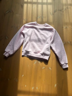 Ljusrosa sweatshirt från gina  - En enkel och stilren ljusrosa sweatshirt med rund hals och ribbade muddar vid ärmar och nederkant. Perfekt för en avslappnad och trendig look. Materialet känns mjukt och bekvämt mot huden.