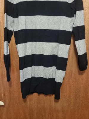 Svart och grå randig tröja Nystad - Stickad tröja från jyshi med breda svarta och grå ränder. Tröjan har rund halsringning och långa ärmar. Perfekt för dig som gillar en enkel men snygg stil. Materialet känns mjukt och bekvämt.