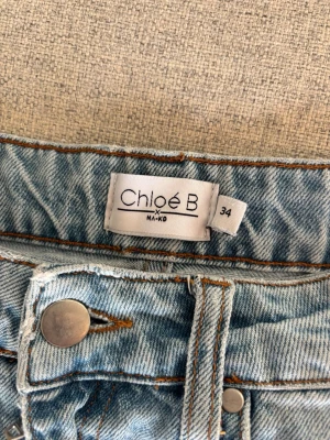 Ljusblå raka jeans Chloé B x NA-KD - Säljer ett par ljusblå raka jeans från Chloé B x NA-KD i storlek 34. Jeansen har klassisk femficksmodell, hög midja och råa, fransiga benslut för en trendig look. Perfekta till sneakers eller boots.