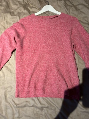 Rosa stickad tröja från Vero Moda - Mysig rosa stickad tröja från Vero Moda med rund halsringning och ribbade muddar vid ärmslut och nederkant. Perfekt för kyliga dagar och enkel att matcha med jeans eller kjol. Materialet är mjukt och bekvämt.